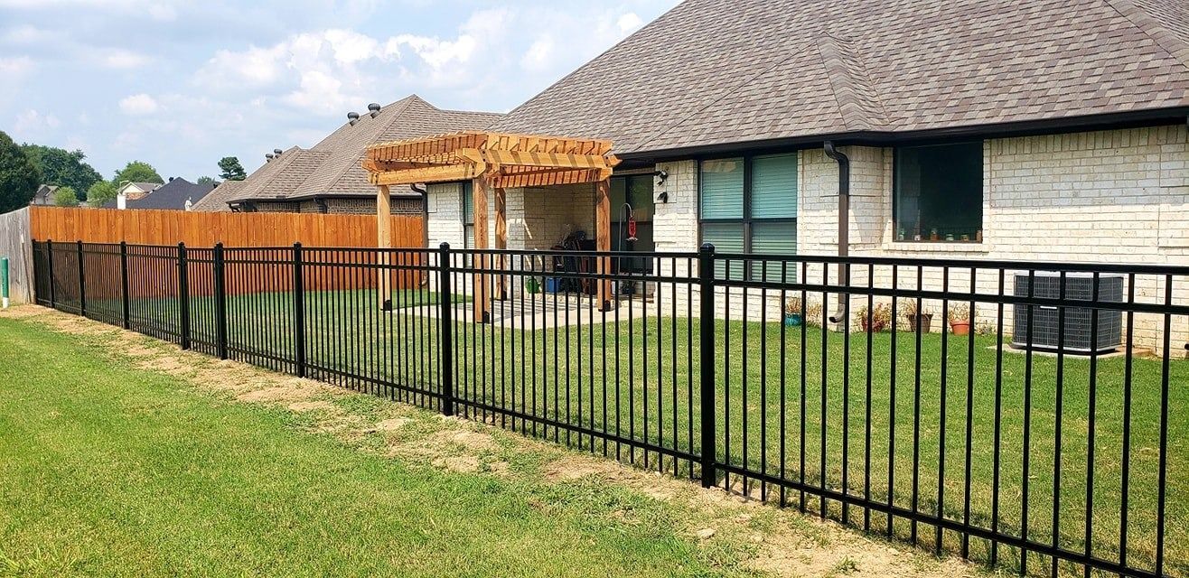Single-story house with a large shingled roof, black fence, and green lawn under a clear sky