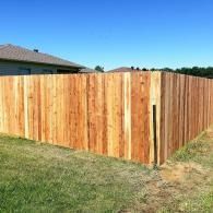Wooden privacy fence enclosing a grassy backyard under a clear blue sky