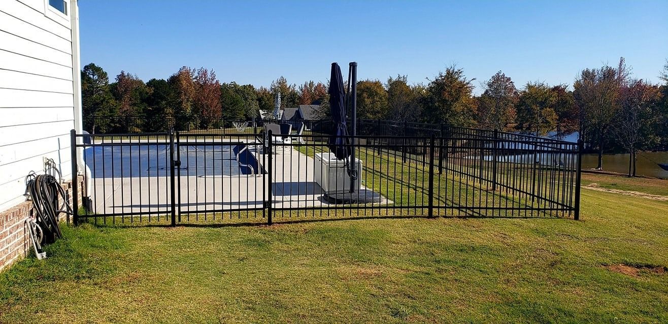 Outdoor fenced concrete pad beside a white building, with grass and trees in the background