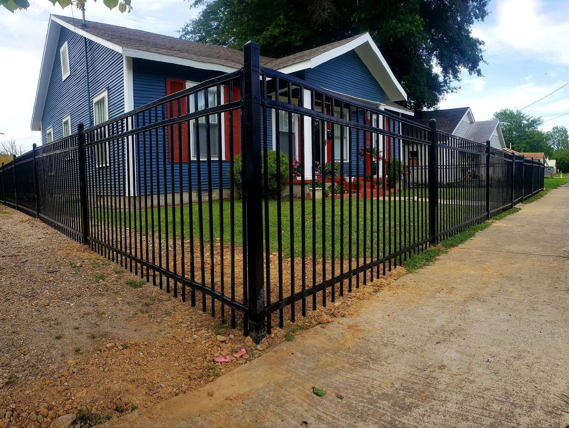 Black metal fence around a blue house with red-trimmed windows beside a gravel road