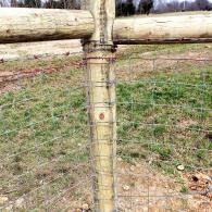 Wooden fence post with wire mesh and a horizontal rail in a grassy field