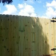 Wooden fence under a blue sky with clouds and sunlight casting shadows