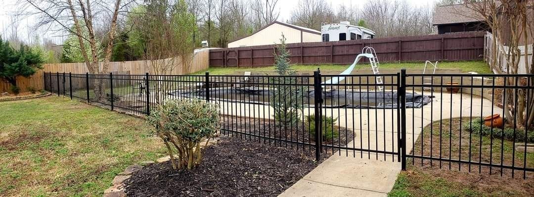 Black metal fence along a sidewalk beside a garden and yard with houses in the background