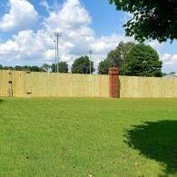 Grassy yard with a wooden fence and brick column under a blue sky with clouds