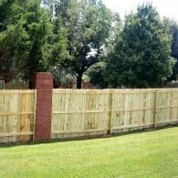 Wooden fence with brick posts along a grassy yard, with trees in the background.