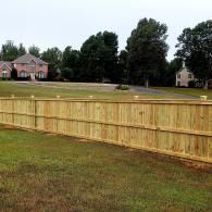 Wooden privacy fence across a grassy field with houses and trees in the background