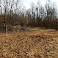 Muddy field with leafless trees and two small metal frames in the background