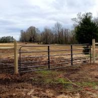 Rustic metal gate on a wooden fence in a muddy field under an overcast sky