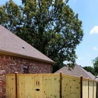 Brick house with wooden fence and tall tree under a blue sky