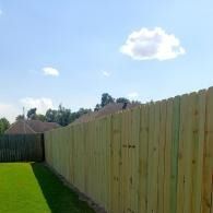 Wooden fence along a green lawn under a blue sky with a few clouds