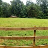 Wooden fence in front of a green field with trees in the background