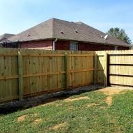 Wooden backyard fence with gate in front of a house and grassy yard