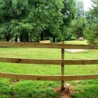 Wooden fence in a grassy park with tall green trees in the background
