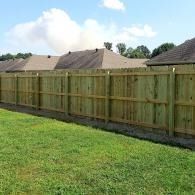 Wooden fence bordering a green grassy yard with houses and a cloudy sky in the background