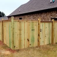 Wooden backyard privacy fence with a gate beside a brick house and grassy yard