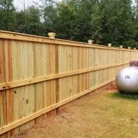 Wooden privacy fence in a backyard with a large silver propane tank nearby.