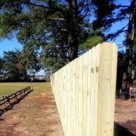 Tall pale wooden fence panel in a sunny yard with trees and a bench in the background