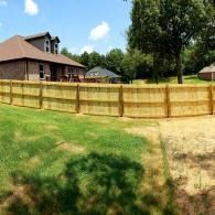 Backyard with a tan wooden fence, green lawn, and a brick house under a blue sky