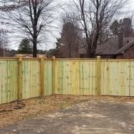 Wooden privacy fence around a driveway with leafless trees and houses in the background
