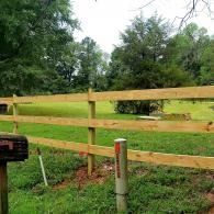 Wooden fence beside a grassy yard with trees and a mailbox in the foreground
