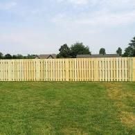Yellow wooden fence across a grassy backyard under a partly cloudy sky.