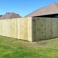 Freshly installed light wood privacy fence beside a house on a grassy lawn