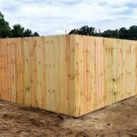 Wooden privacy fence corner surrounding a dirt yard under a cloudy sky