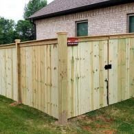 Wooden privacy fence enclosing a backyard beside a brick house, with a gate and latch.