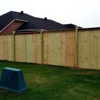 Backyard with a wooden privacy fence and a blue utility box on the grass.