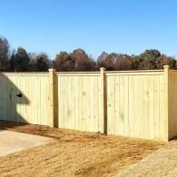 Light wood privacy fence with posts in a grassy yard under a clear blue sky