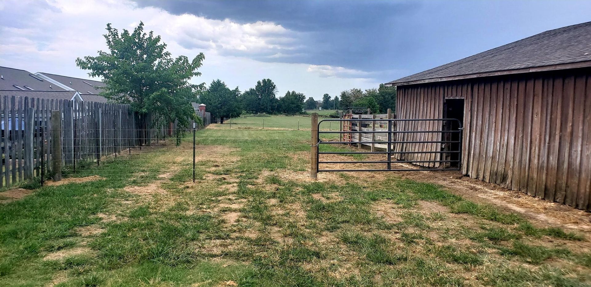 Farmyard path between a wooden fence and barn under a cloudy sky