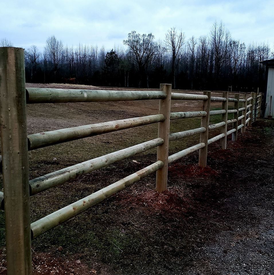 Wooden fence along a gravel path beside an open field under a cloudy sky