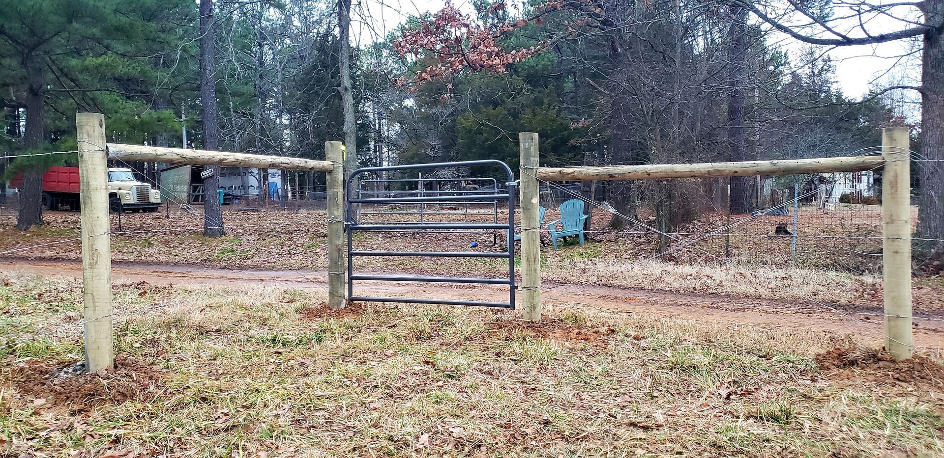 Wooden gate in a leaf-covered yard with trees and a fence in the background