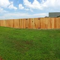 Green grassy yard with a wooden fence under a partly cloudy sky