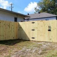 Wooden fence and gate in a backyard with a grassy yard and neighboring houses behind it