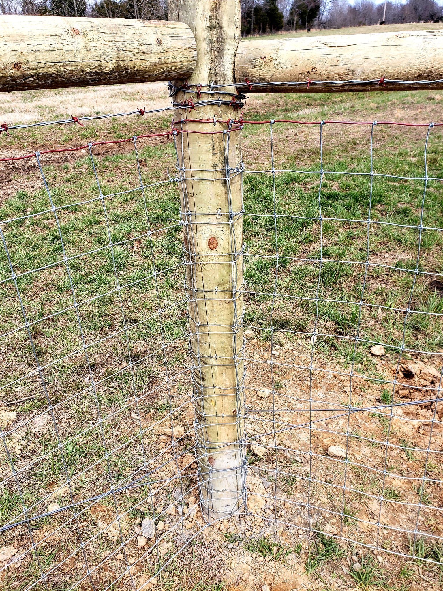 Close-up of a weathered wooden fence post with horizontal rails and wire mesh over patchy grass.