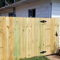 Wooden privacy fence with black hinges and latch beside a white house and grassy yard