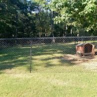 Backyard with chain-link fence, grassy lawn, trees, and a small brick fire pit