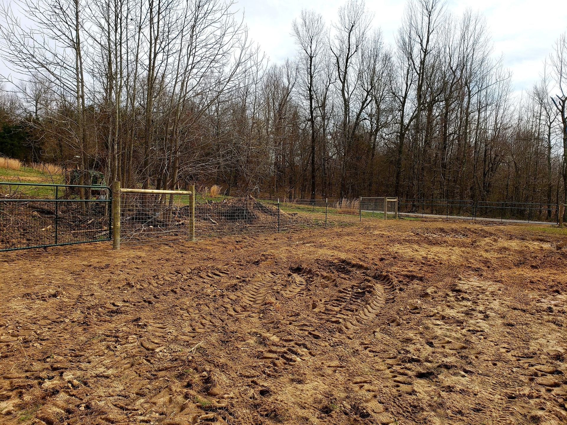 Freshly tilled brown field bordered by leafless trees and a wire fence on an overcast day