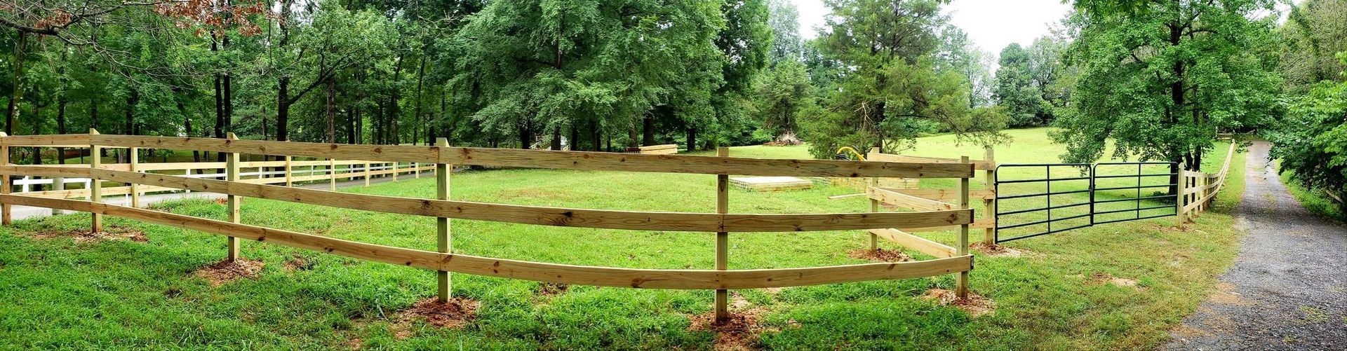 Wooden fence beside a grassy field and trees, with a gravel path on the right.