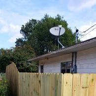 Wooden fence beside a house with a satellite dish and trees in the background