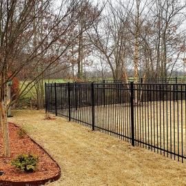 Black metal fence along a curved gravel path beside bare trees and a landscaped garden border