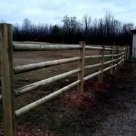 Wooden fence along a grassy field with leafless trees in the background