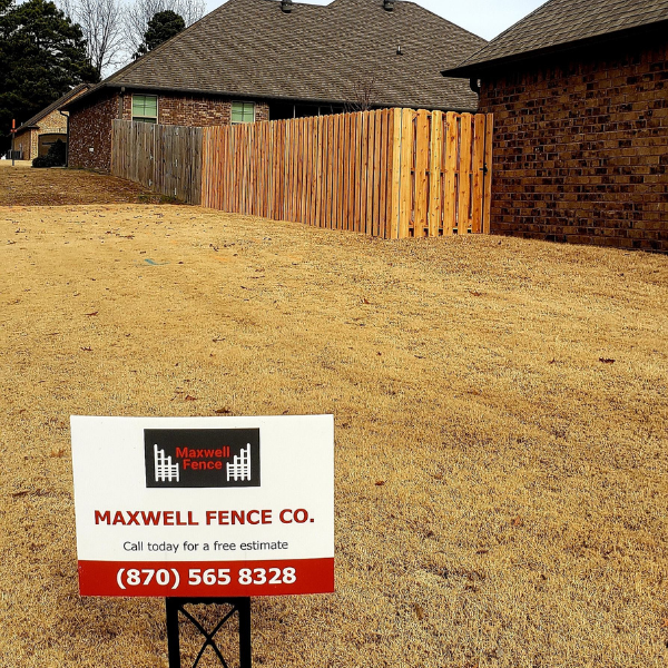 Wooden privacy fence beside a brick house, with Maxwell Fence Co. sign in the yard.