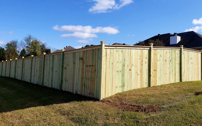 Wooden fence lining a grassy yard under a blue sky, with houses in the background.
