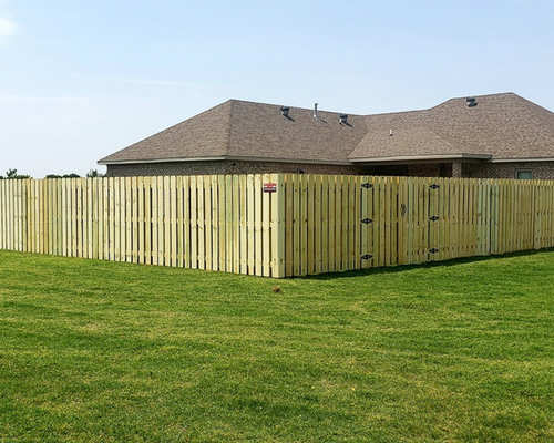 Backyard with wooden privacy fence around a grassy lawn beside a tan house