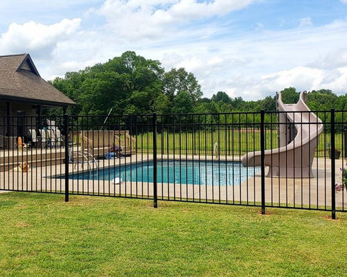 Backyard pool with black fence, stone patio, and beige water slide beside a house