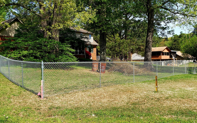 Chain-link fence around a grassy yard with trees and houses in the background.