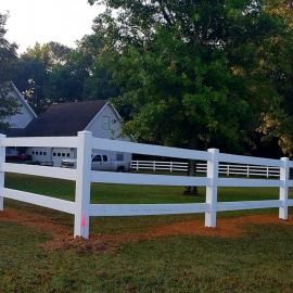 White fenced yard with a white house and large trees in the background
