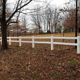 White fence along a leaf-covered yard with bare trees on a cloudy day